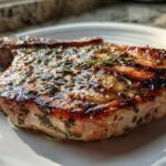 Close-up of a perfectly grilled pork chop coated in a glistening herb marinade for pork chops.