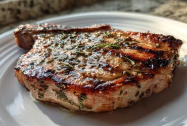 Close-up of a perfectly grilled pork chop coated in a glistening herb marinade for pork chops.