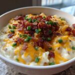 A close-up of a hearty bowl of loaded potato soup recipe topped with melted cheddar cheese, bacon bits, and green onions.