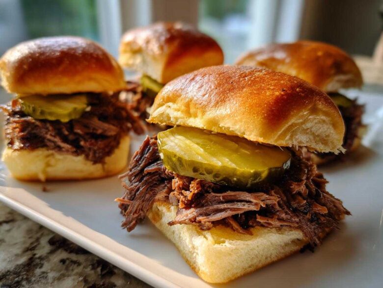 Four delicious Mississippi pot roast sliders piled high with shredded beef and topped with a thick pickle slice on brioche buns.