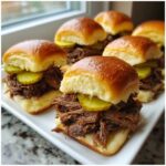 A close-up of several Mississippi pot roast sliders filled with shredded beef and pickles on shiny brioche buns.