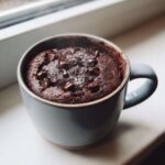 Close-up of a steaming chocolate mug cake topped with chocolate chips and sea salt.