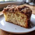 Close-up of a moist slice of coffee cake with a thick, sugary cinnamon crumb topping and light glaze.