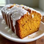 A close-up of a slice of moist sweet potato pound cake topped with a thick white glaze and orange zest.