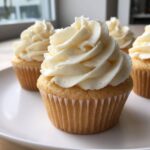 Close-up of moist vanilla cupcakes topped with perfectly swirled white vanilla buttercream frosting.