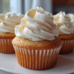 Close-up of three moist vanilla cupcakes topped with tall swirls of white buttercream frosting.
