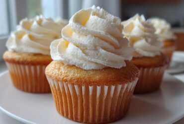 Close-up of three moist vanilla cupcakes topped with tall swirls of white buttercream frosting.