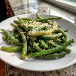 A close-up of roasted green beans topped with grated Parmesan cheese on a white plate.