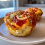 Two golden brown Pizza muffins topped with melted mozzarella cheese and tomato sauce, sprinkled with herbs.