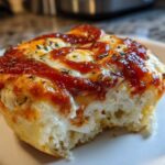 Close-up of a single, fluffy pizza muffin with melted cheese, tomato sauce, and herbs, showing a bite taken out.