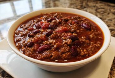 A close-up of a white bowl filled with rich, hearty crockpot chili featuring ground meat and kidney beans.
