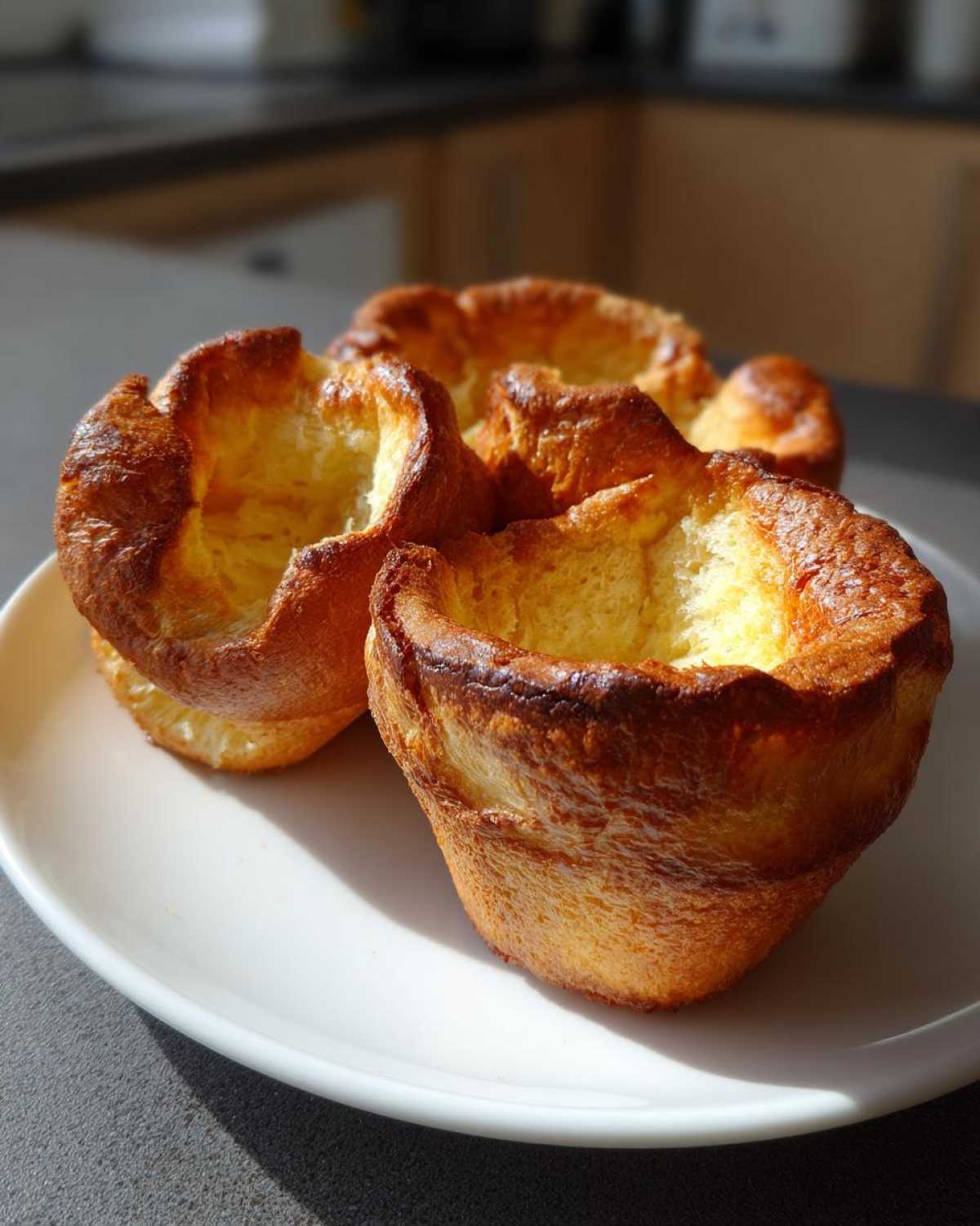 Three golden brown, perfectly risen Yorkshire puddings sitting on a white plate.