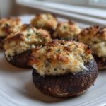 Close-up of perfectly baked Sausage Stuffed Mushrooms with golden-brown, cheesy topping on a white platter.