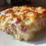 Close-up of a square serving of creamy scalloped potatoes and ham with a golden-brown, cheesy baked top.