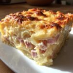 A close-up of a thick, square slice of cheesy scalloped potatoes and ham with a golden-brown, bubbly top.