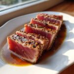Five thick slices of seared tuna steak, coated in a sesame seed crust, resting in a rich marinade for tuna steak sauce.