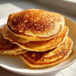 A close-up stack of four fluffy, golden-brown sourdough pancakes drizzled with syrup.