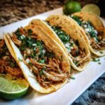 Four soft corn chicken tacos filled with shredded seasoned meat, topped with diced onion and cilantro, served with lime wedges.