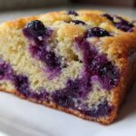 Close-up of a moist slice of blueberry banana bread showing bright purple blueberries baked into the yellow crumb.