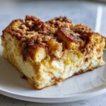 A close-up of a decadent slice of french toast casserole featuring a thick cream cheese layer and cinnamon streusel topping.