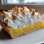 A close-up slice of lemon meringue pie showing bright yellow curd, flaky crust, and peaks of perfectly browned meringue.
