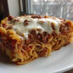 A thick slice of baked spaghetti pie topped with meat sauce and melted mozzarella cheese.