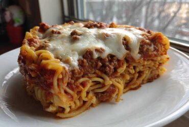 A thick slice of baked spaghetti pie topped with meat sauce and melted mozzarella cheese.
