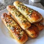 A close-up of several soft, golden breadsticks generously brushed with melted garlic butter and parsley.