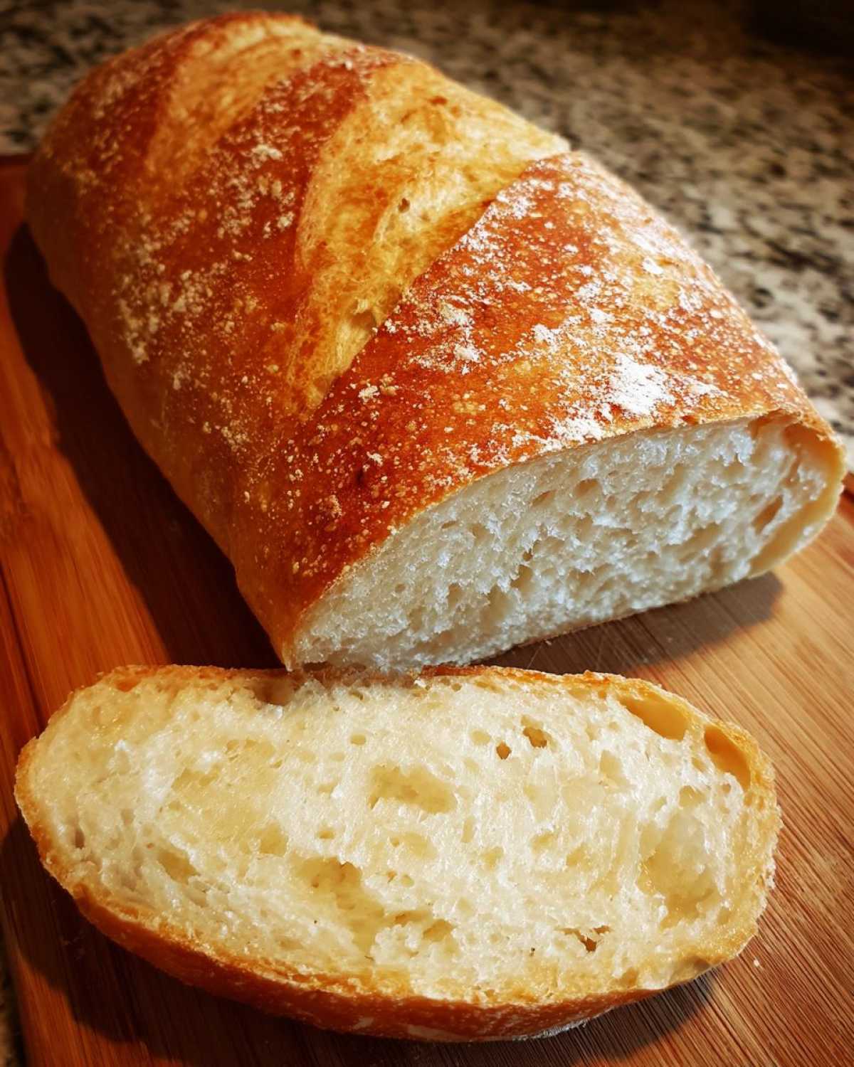 A golden-crusted loaf of soft french bread, partially sliced to show the airy interior texture.
