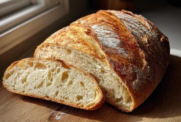 A loaf of golden-crusted french bread, partially sliced, showing a soft, airy interior crumb.