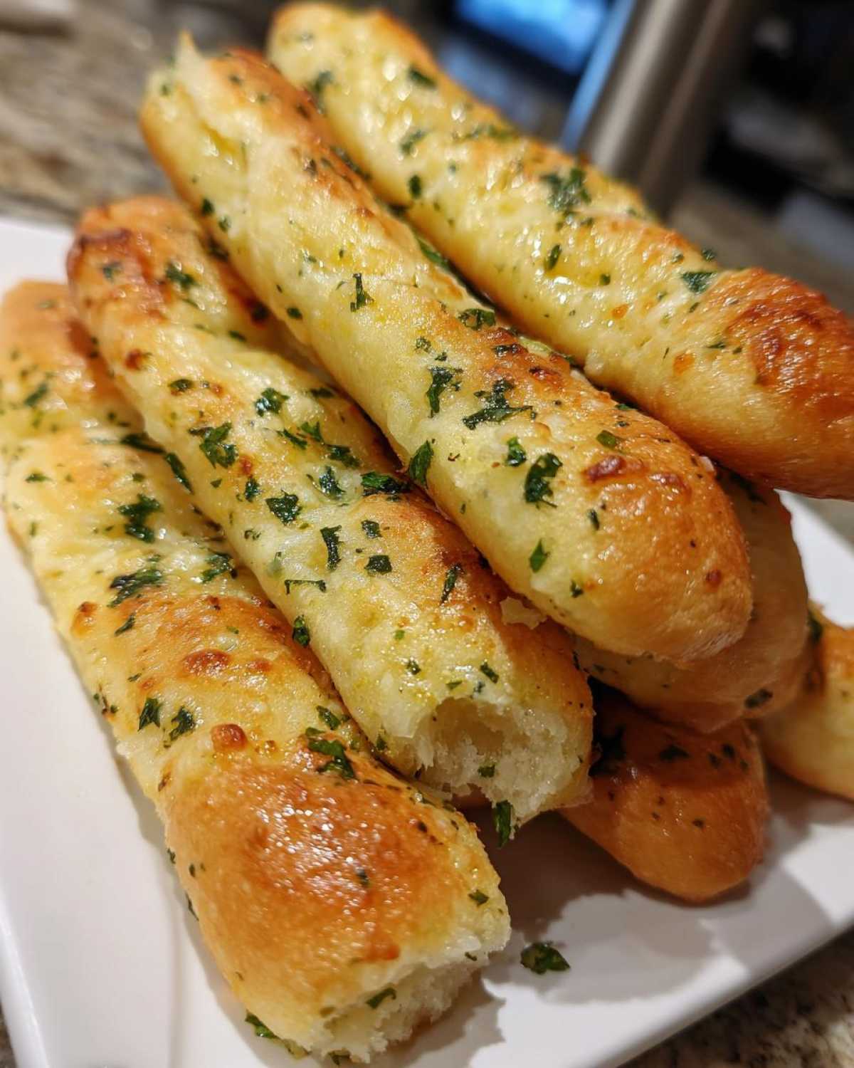 A close-up stack of freshly baked, soft breadsticks brushed with garlic butter and sprinkled with parsley.