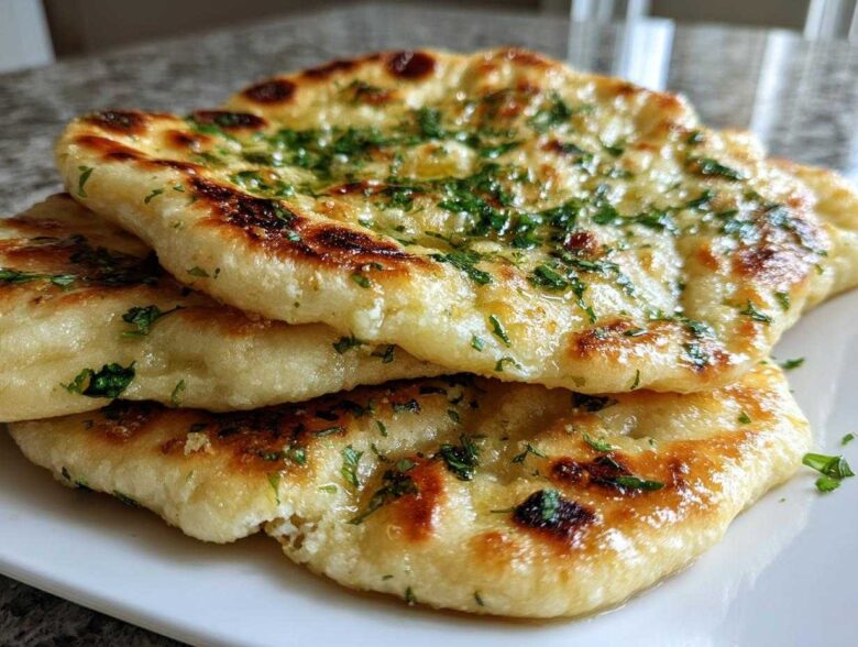 Close-up of a stack of three soft, golden-brown naan bread pieces brushed with butter and sprinkled with fresh parsley.
