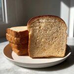 A close-up of soft, fluffy slices of whole wheat bread stacked on a plate, highlighted by sunlight.