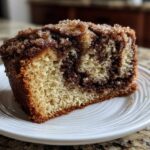 A close-up of a moist slice of sour cream coffee cake featuring a rich cinnamon swirl and sugary crumb topping.