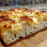 Close-up cross-section showing the airy crumb structure of sourdough discard pizza dough topped with melted, browned cheese.