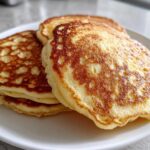 A stack of three golden-brown sourdough pancakes with lacy edges resting on a white plate.