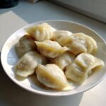A close-up of several freshly steamed Traditional Chinese Dumplings piled on a white plate, highlighted by natural sunlight.