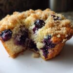 Close-up of a delicious blueberry muffin cut in half showing moist interior, bursting blueberries, and crumb topping.