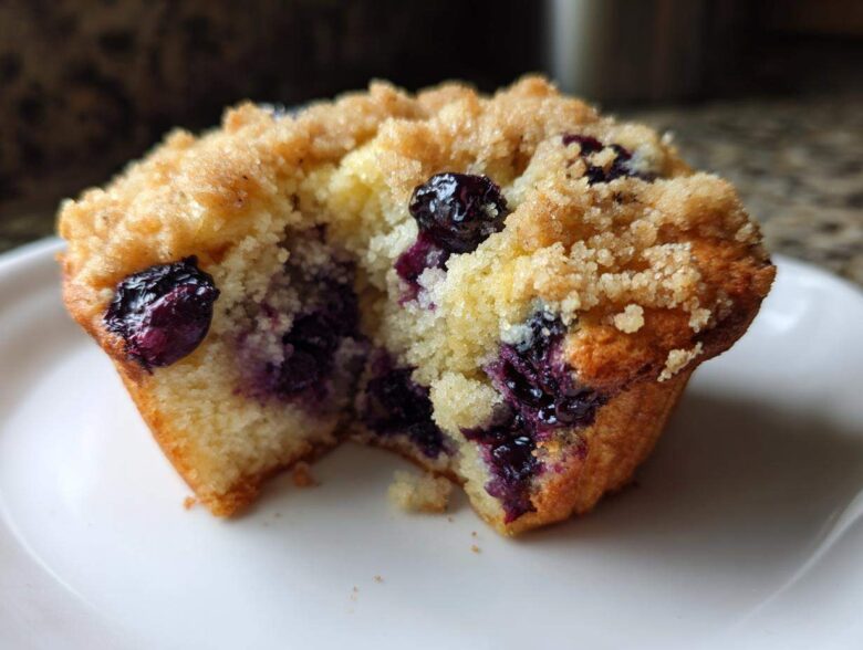 Close-up of a delicious blueberry muffin cut in half showing moist interior, bursting blueberries, and crumb topping.