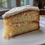 Close-up of a moist slice of vanilla cake with white frosting, showing the crumb texture.