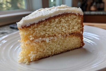 Close-up of a moist slice of vanilla cake with white frosting, showing the crumb texture.