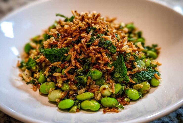 A vibrant serving of crispy rice salad featuring bright green edamame, fresh mint, and a generous topping of crispy fried rice.