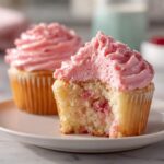 Close-up of a 350-calorie strawberry cupcake with a bite taken out, revealing pink frosting and strawberry pieces in the cake.