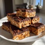 A stack of homemade, no-bake protein bars featuring an oat base and a thick chocolate topping.