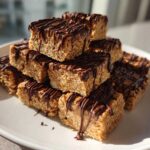 A stack of homemade 5-ingredient protein bars drizzled generously with melted dark chocolate on a white plate.
