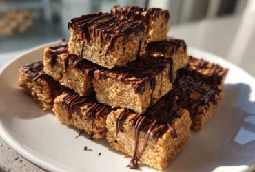 A stack of homemade 5-ingredient protein bars drizzled generously with melted dark chocolate on a white plate.