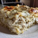 A close-up of a thick, layered slice of white chicken lasagna topped with melted, browned cheese and herbs.