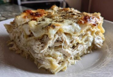 A close-up of a thick, layered slice of white chicken lasagna topped with melted, browned cheese and herbs.