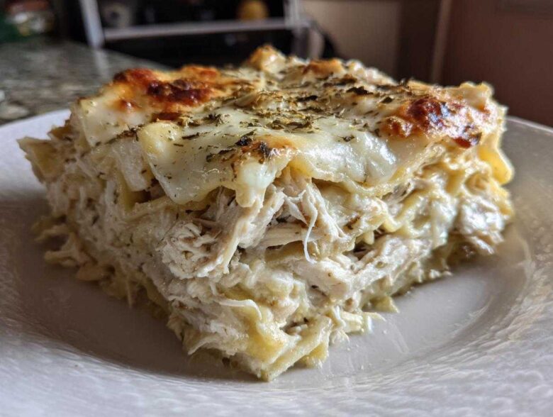 A close-up of a thick, layered slice of white chicken lasagna topped with melted, browned cheese and herbs.