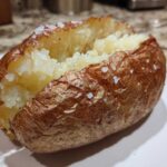 A perfectly cooked air fryer baked potato, split open to show fluffy insides and a crispy, salted skin.